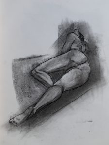 A heavily foreshortened charcoal drawing of a nude man lying down, from behind.
